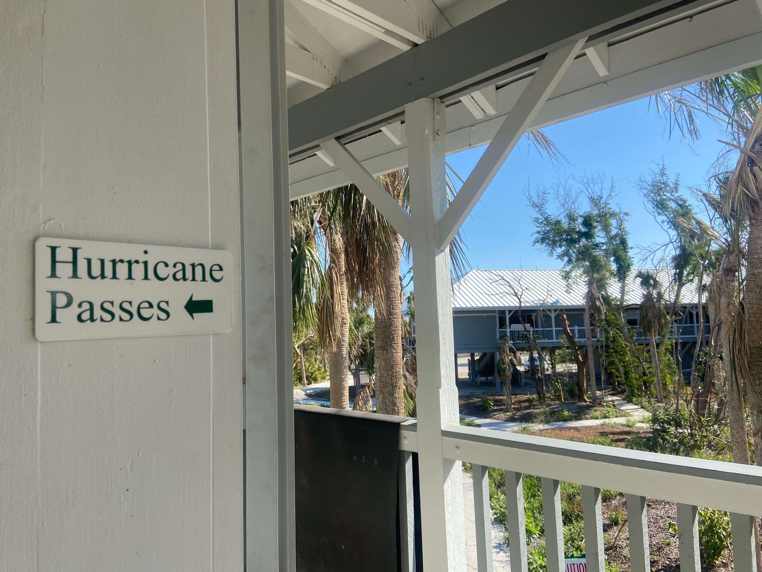 Un letrero blanco con letras negras que dice 'Pases de Huracán' cuelga afuera del Ayuntamiento de Sanibel. Los daños causados por los vientos del Huracán Ian se pueden ver en los árboles destruidos en el fondo. Las autoridades de Sanibel limitaron el acceso a la comunidad adinerada emitiendo pases de huracán para los trabajadores de restauración.(María Inés Zamudio/ Center for Public Integrity)