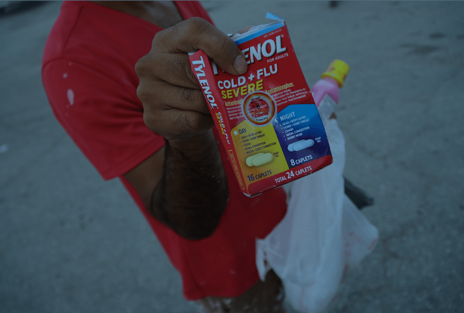 Un trabajador con camiseta roja muestra en su mano una caja de Tylenol Cold+Flu, y una botella de Pepto Bismol. El trabajador está en un estacionamiento conocido en Fort Myers donde trabajadores se congregan a esperar a que los recojan para trabajar limpiando escombros de las estructuras que fueron destruidas por el huracán Ian. (Jiahui Huang/Columbia Journalism Investigations)