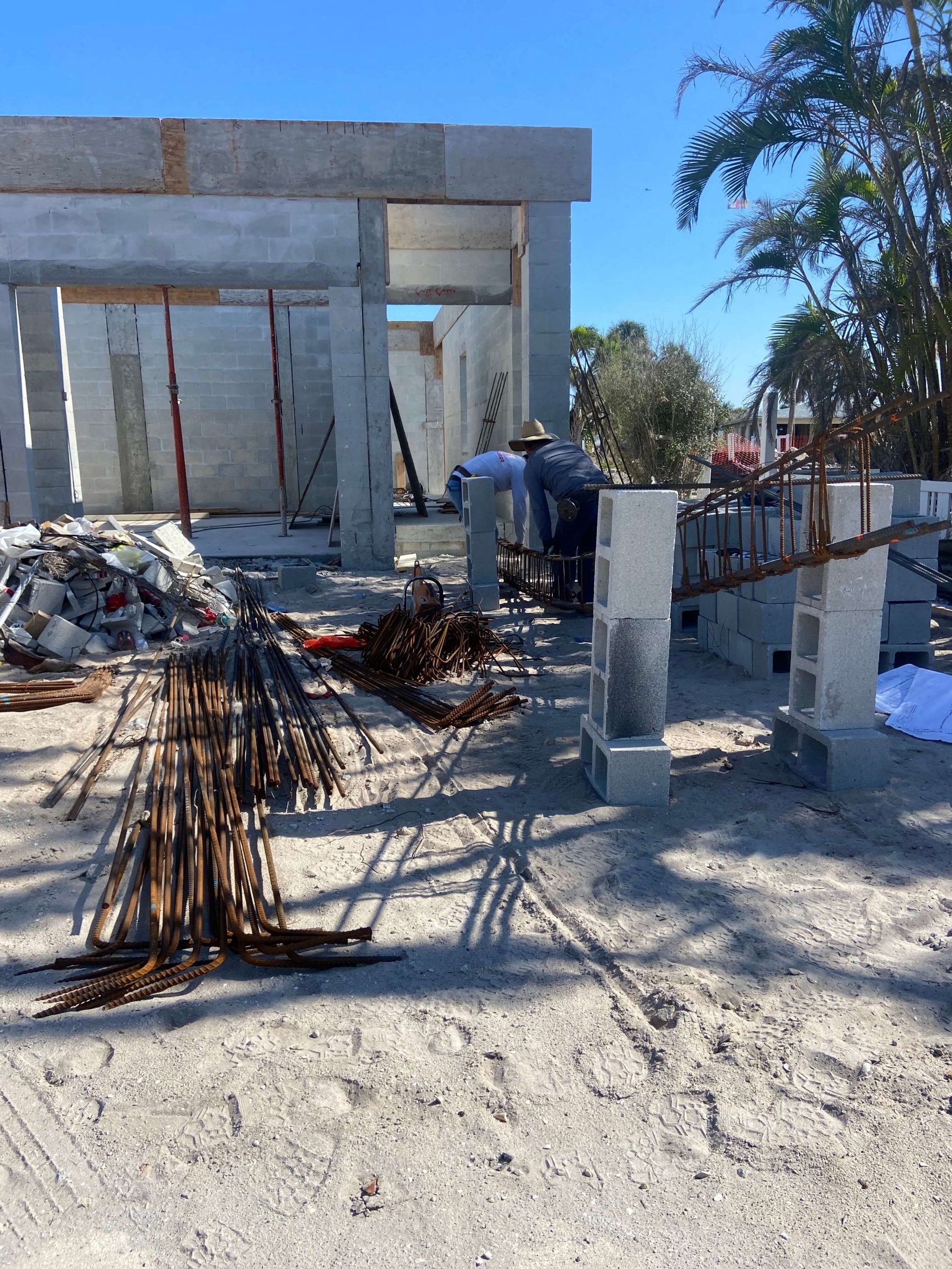 Dos trabajadores construyen una casa que fue destruida por el Huracán Ian en la Isla Sanibel, casi seis meses antes. La estructura de concreto se puede ver en el fondo mientras dos hombres trabajan sin equipo de protección. Meses después del huracán, llegaron docenas de trabajadores de restauración para limpiar escombros, demoler y reconstruir (María Inés Zamudio / Center for Public Integrity)
